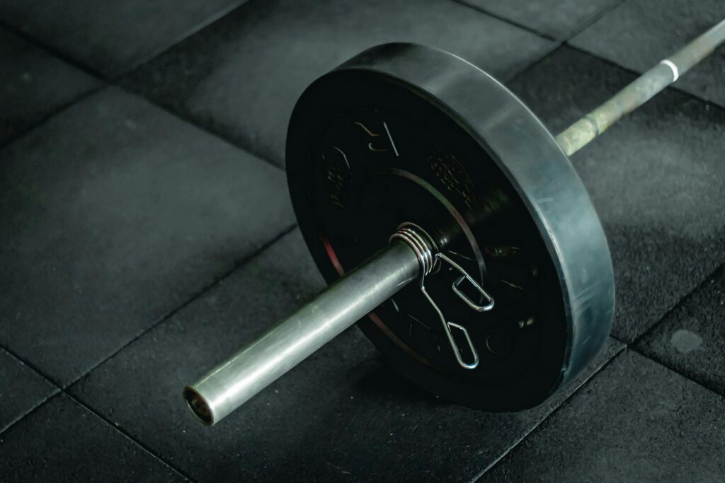 Detailed view of a barbell with heavy weights resting on a dark gym floor mat.